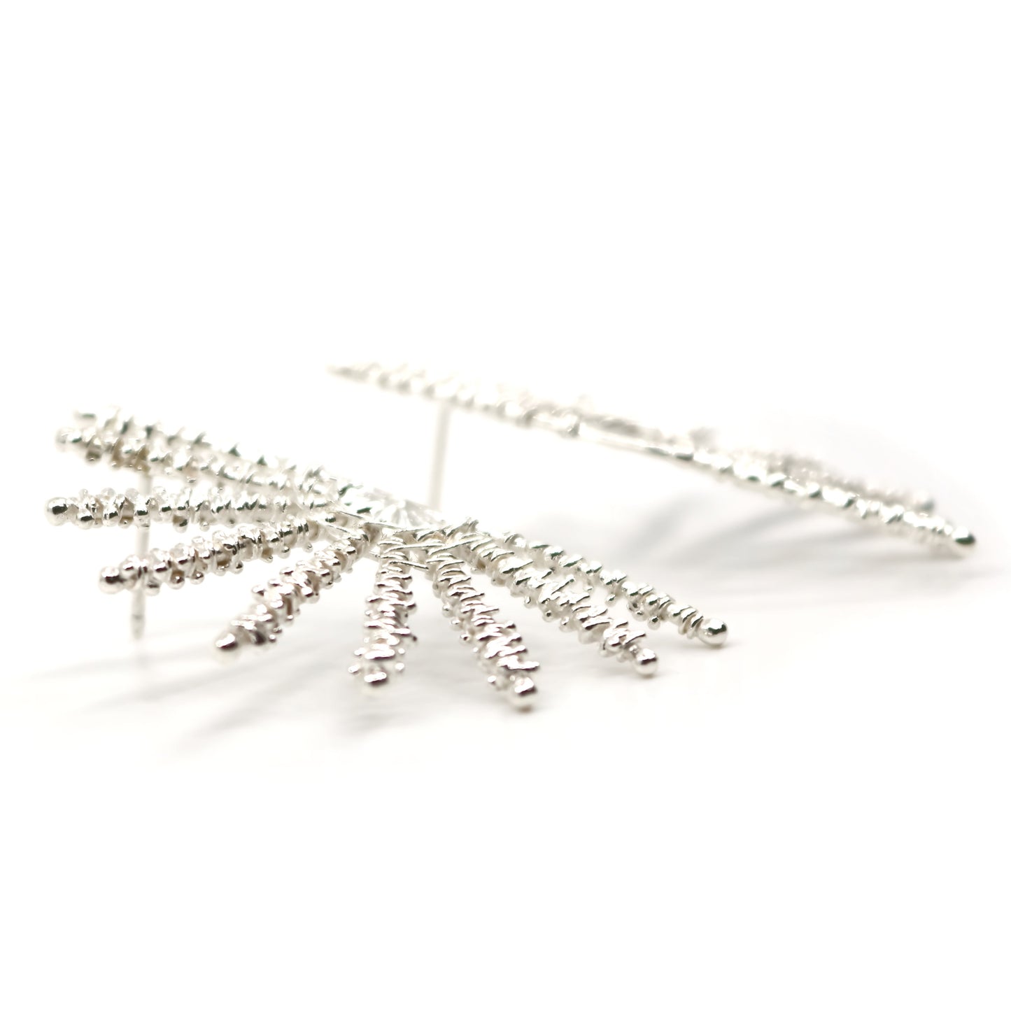 Side view of silver sunray shaped earrings on a white background